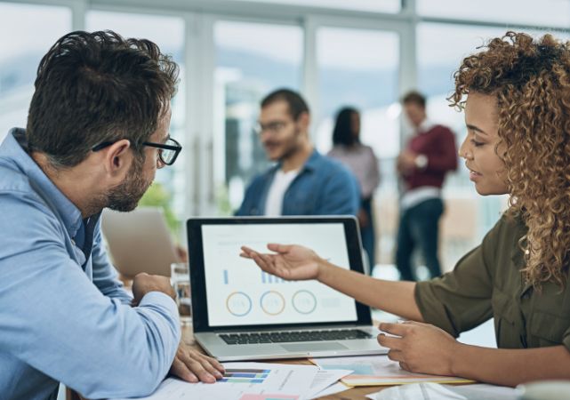Two professionals reviewing a laptop dashboard together in a meeting.